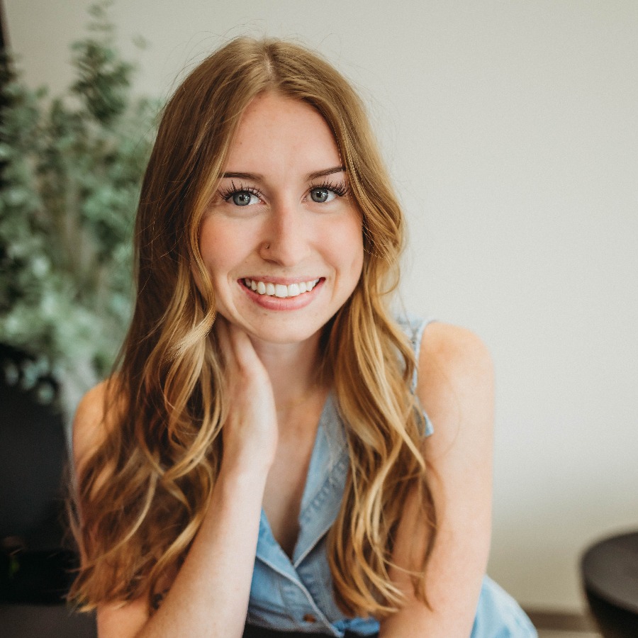 Woman with long hair resting her head on her hand and smiling at the camera.