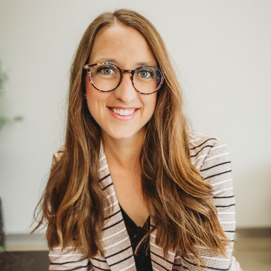 Woman with long light brown hair and glasses smiling.