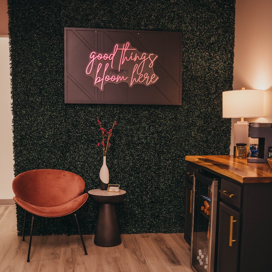 Corner of a room with a neon sign and a coffee bar with a grassy backdrop.