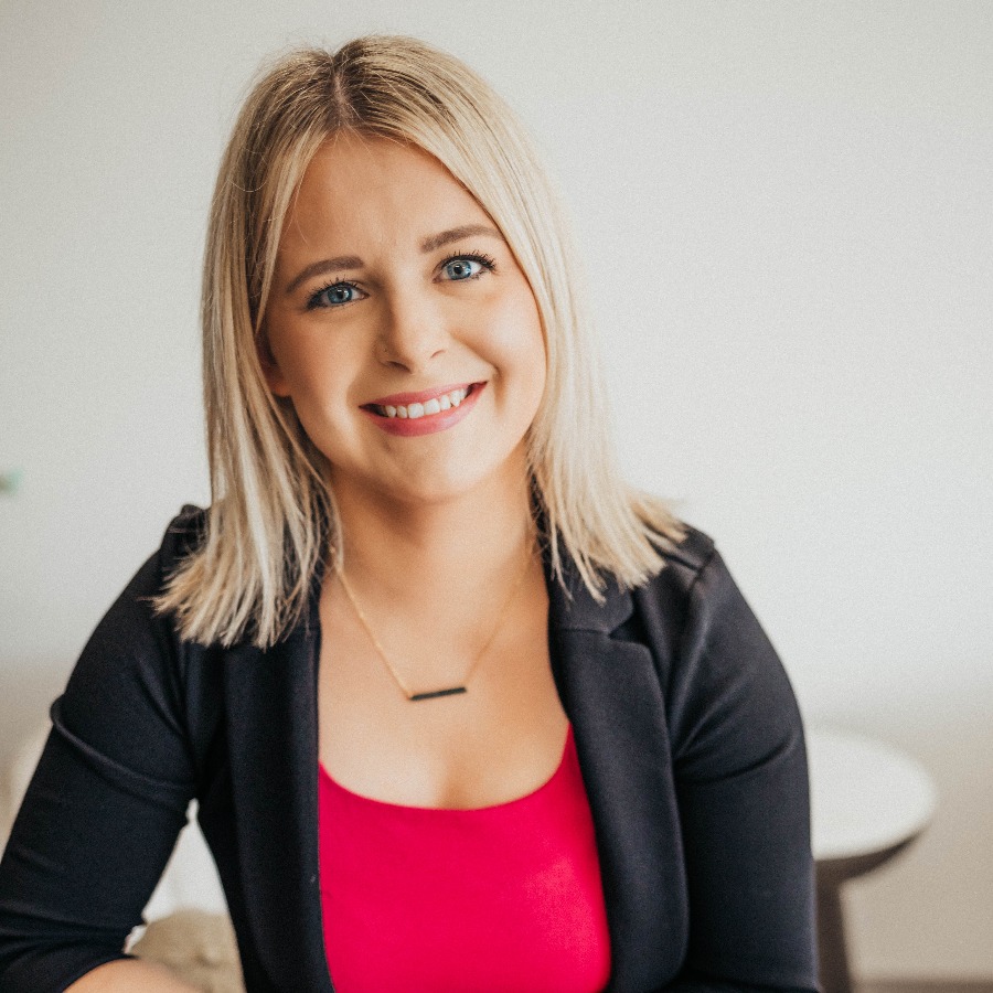 Blonde woman leaning against a counter smiling.