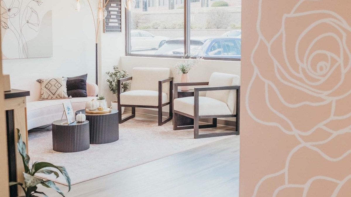 View of a waiting room with a sofa and two chairs in bright natural lighting.