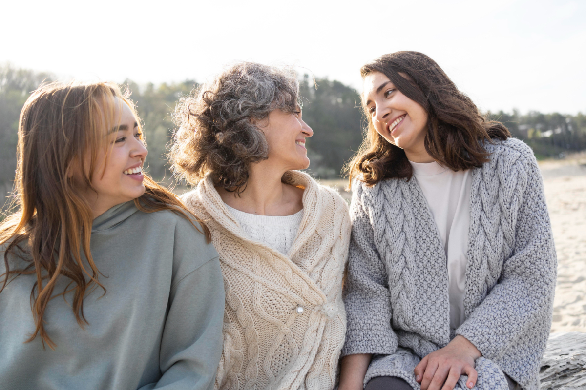 Three women smiling at each other outdoors.